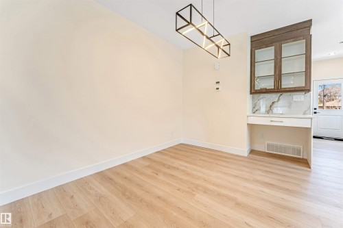 Light wood-finish flooring with white baseboards, a built-in cabinet with glass doors, a stone countertop, and a contemporary linear light fixture - 10323 79 Street, Edmonton, AB - Indoor Photo Showing Other Room