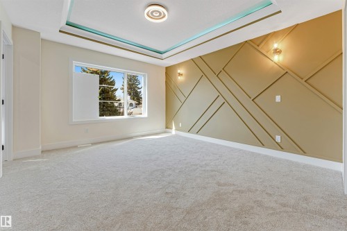 Spacious interior featuring a decorative accent wall with geometric molding, recessed ceiling with a teal and gold trim, light beige wall paint, plush carpeting, and a large window - 10323 79 Street, Edmonton, AB - Indoor Photo Showing Other Room