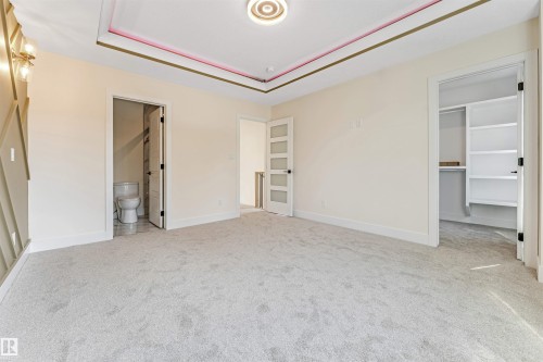 Spacious carpeted room featuring a decorative tray ceiling with recessed lighting, an adjacent built-in closet with shelving, and a nearby bathroom with a toilet and tiled walls - 10323 79 Street, Edmonton, AB - Indoor Photo Showing Other Room