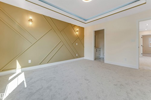 Spacious room featuring a decorative accent wall with geometric paneling, two wall-mounted sconces, and a tray ceiling with recessed lighting - 10323 79 Street, Edmonton, AB - Indoor Photo Showing Other Room