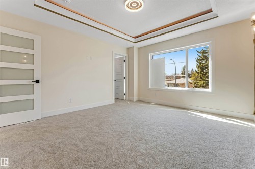 Spacious room featuring neutral carpeting, a large window, and a decorative tray ceiling with recessed lighting - 10323 79 Street, Edmonton, AB - Indoor Photo Showing Other Room