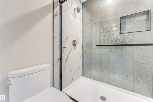 Contemporary shower enclosure featuring a clear glass door with black framing, complemented by textured gray wall tiling and a built-in shower niche - 10323 79 Street, Edmonton, AB - Indoor Photo Showing Bathroom