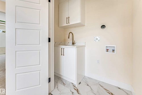 Dedicated laundry space featuring marble-look tile flooring, white shaker cabinetry, a brass-tone faucet, and a wall-mounted utility sink - 10323 79 Street, Edmonton, AB - Indoor Photo Showing Other Room
