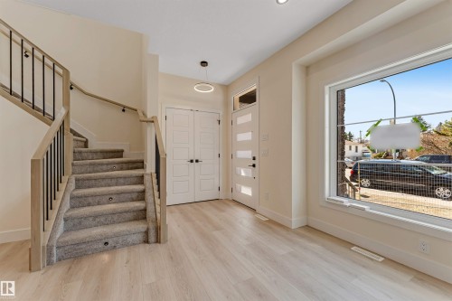 Foyer featuring light wood-finish flooring, a contemporary staircase with carpeted treads and black metal balusters, a large picture window, and a modern entryway door with frosted glass panels - 10323 79 Street, Edmonton, AB - Indoor Photo Showing Other Room