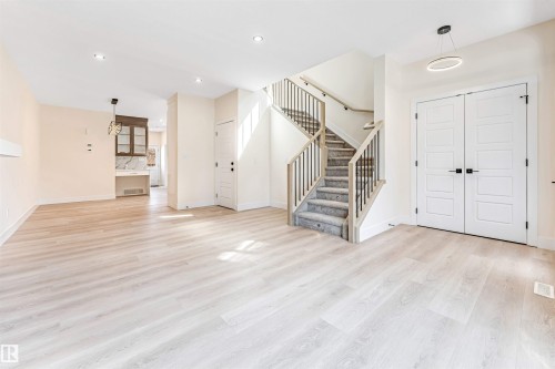 Bright main living area featuring light wood-finish flooring, a contemporary staircase with carpeted treads and dark metal spindles, and a double-door entry - 10323 79 Street, Edmonton, AB - Indoor Photo Showing Other Room