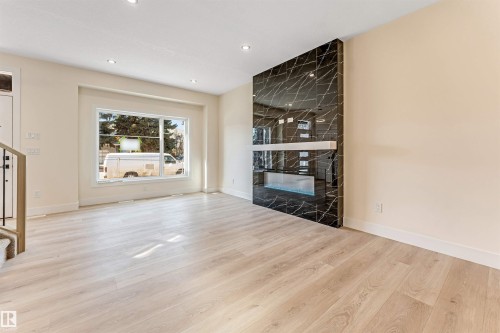 Spacious room featuring light wood-finish flooring, recessed lighting, and a prominent black patterned accent wall - 10323 79 Street, Edmonton, AB - Indoor Photo Showing Living Room With Fireplace