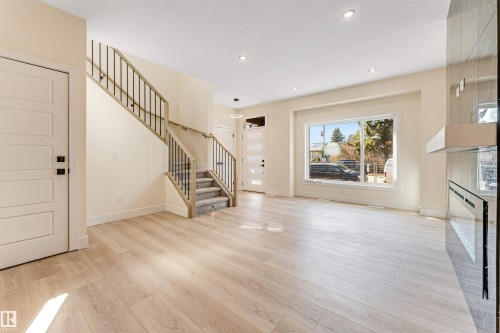 Spacious living area featuring light wood-finish flooring, recessed lighting, and a prominent staircase with wood railings and black spindles - 10323 79 Street, Edmonton, AB - Indoor