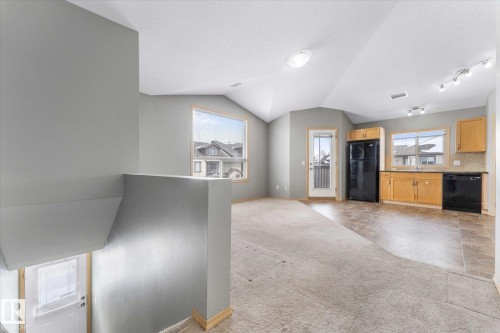 Kitchen featuring light wood cabinetry, black appliances, track lighting, a window over the sink, and an arched doorway - 86 604 62 Street, Edmonton, AB - Indoor Photo Showing Kitchen With Double Sink