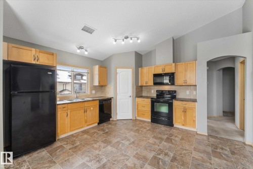 Kitchen featuring wood cabinetry, black appliances, a double basin sink, and a tile backsplash - 86 604 62 Street, Edmonton, AB - Indoor Photo Showing Kitchen With Double Sink