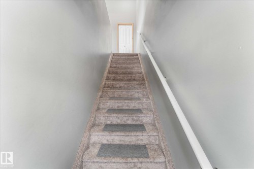 Carpeted room featuring a large window with natural wood trim, vaulted ceilings, and a light gray color palette - 86 604 62 Street, Edmonton, AB - Indoor Photo Showing Other Room