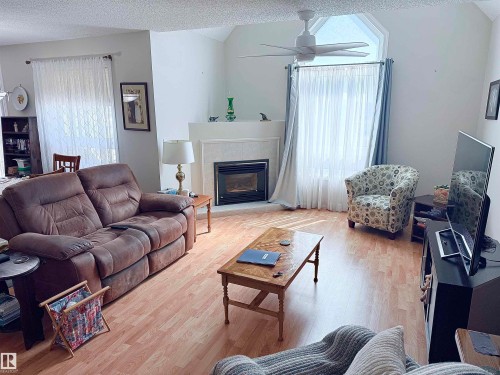 Living area featuring vaulted ceilings, wood-finish flooring, a fireplace with a tiled surround and mantel, a ceiling fan, and large windows with treatments - 410 9926 100 Avenue, Fort Saskatchewan, AB - Indoor Photo Showing Living Room With Fireplace