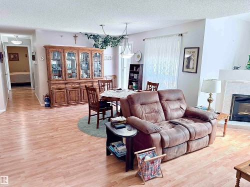 Open-concept living space featuring wood-finish flooring, a fireplace with a light-toned surround, and a dining area with a chandelier - 410 9926 100 Avenue, Fort Saskatchewan, AB - Indoor Photo Showing Living Room With Fireplace