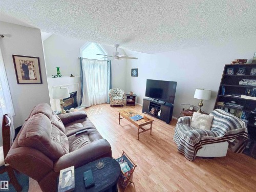 Living area featuring vaulted ceilings, wood-finish flooring, a fireplace with a white mantel, and a ceiling fan - 410 9926 100 Avenue, Fort Saskatchewan, AB - Indoor Photo Showing Living Room With Fireplace