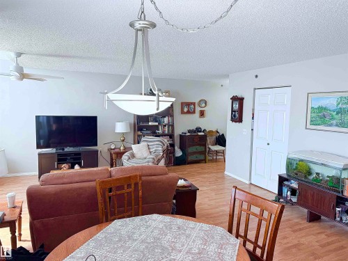 Open-concept living area featuring wood-finish flooring, a white ceiling fan, and a contemporary chandelier - 410 9926 100 Avenue, Fort Saskatchewan, AB - Indoor
