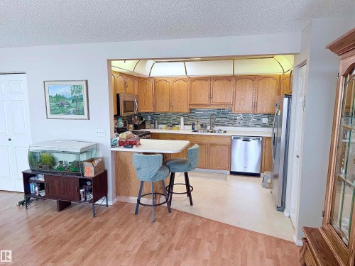 Kitchen featuring wood-finish cabinetry, stainless steel appliances, and a tiled backsplash - 410 9926 100 Avenue, Fort Saskatchewan, AB - Indoor Photo Showing Kitchen With Double Sink