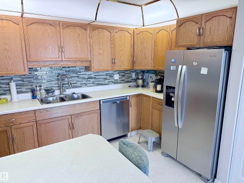 Kitchen featuring light wood cabinetry, white countertops, and a full-height glass mosaic tile backsplash - 410 9926 100 Avenue, Fort Saskatchewan, AB - Indoor Photo Showing Kitchen With Double Sink