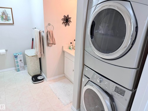 Dedicated laundry area featuring a stacked washer and dryer, adjacent to a vanity with a white cabinet and countertop - 410 9926 100 Avenue, Fort Saskatchewan, AB - Indoor Photo Showing Laundry Room
