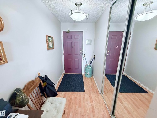 Entryway featuring wood-finish flooring, a flush-mount ceiling light fixture, and a mirrored sliding closet door - 410 9926 100 Avenue, Fort Saskatchewan, AB - Indoor Photo Showing Other Room