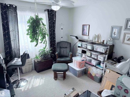 Carpeted room featuring a ceiling fan, a window with sheer and patterned curtains, and a built-in shelving unit - 410 9926 100 Avenue, Fort Saskatchewan, AB - 