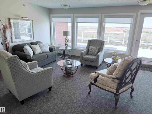 This inviting common area features a wall of floor-to-ceiling windows, offering abundant natural light - 410 9926 100 Avenue, Fort Saskatchewan, AB - Indoor Photo Showing Living Room
