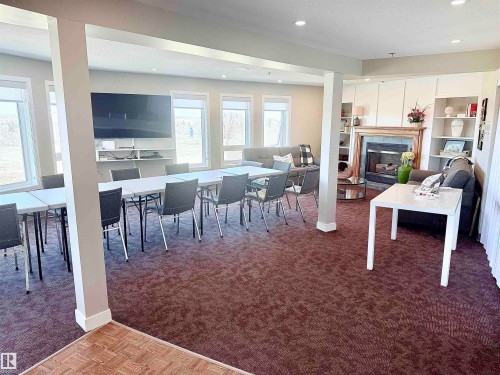 Spacious common area featuring recessed lighting, a fireplace with a stone surround and wood mantle, built-in shelving, and large windows - 410 9926 100 Avenue, Fort Saskatchewan, AB - Indoor With Fireplace