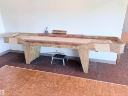 Spacious room featuring a shuffleboard table with a light wood-finish base and a textured playing surface - 