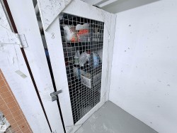 Enclosed storage unit with a white wire mesh door and painted concrete walls - 