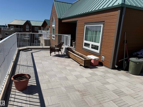 Expansive rooftop patio featuring light-toned square pavers, white perimeter railing, and brown horizontal siding - 410 9926 100 Avenue, Fort Saskatchewan, AB - Outdoor With Exterior