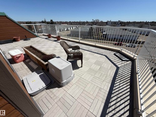 Expansive rooftop deck featuring light-colored square paving, a white perimeter railing, and sloped brown wood-siding exterior walls - 410 9926 100 Avenue, Fort Saskatchewan, AB - Outdoor