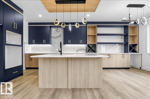 Contemporary kitchen featuring a light wood-finish flooring, a central island with a light wood-finish base, dark blue cabinetry, and a white countertop - 1150 Gyrfalcon Crescent, Edmonton, AB - Indoor Photo Showing Kitchen With Upgraded Kitchen