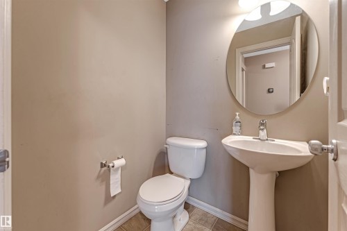 Pedestal sink with chrome faucet, circular mirror, and wall-mounted light fixture - 1431 Hodgson Way, Edmonton, AB - Indoor Photo Showing Bathroom