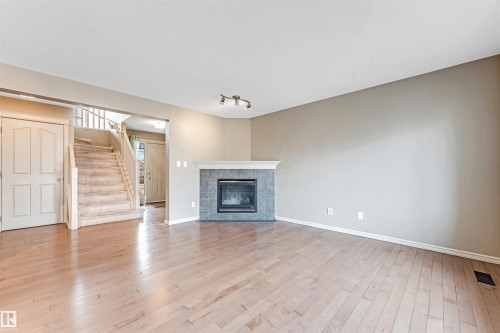 Expansive living area featuring light wood-finish flooring, a tiled fireplace with a mantel, and neutral wall tones - 1431 Hodgson Way, Edmonton, AB - Indoor Photo Showing Living Room With Fireplace