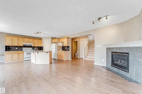 Open-concept living space featuring wood-finish flooring, a kitchen island, track lighting, a gas fireplace with a tiled surround, and a staircase with carpeted treads - 1431 Hodgson Way, Edmonton, AB - Indoor With Fireplace