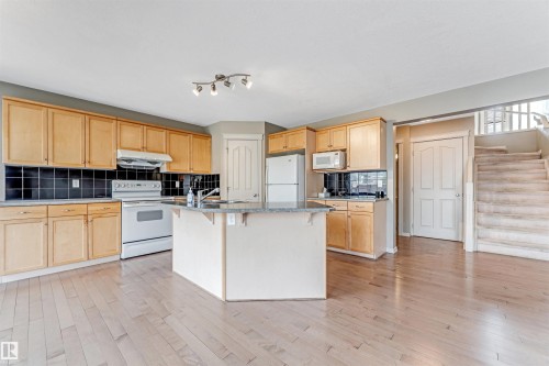 Open-concept kitchen featuring light wood cabinetry, white appliances, a central island with an extended countertop, and dark tile backsplash - 1431 Hodgson Way, Edmonton, AB - Indoor Photo Showing Kitchen With Double Sink