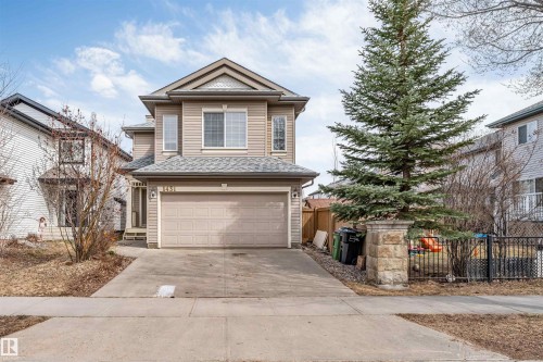 Two-story property with light brown siding, a dual-pane window, an attached garage, a concrete driveway, and a stone column - 1431 Hodgson Way, Edmonton, AB - Outdoor