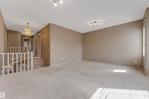 Spacious room featuring neutral carpeting, a staircase with white wood railing, and a decorative chandelier - 1431 Hodgson Way, Edmonton, AB - Indoor Photo Showing Other Room