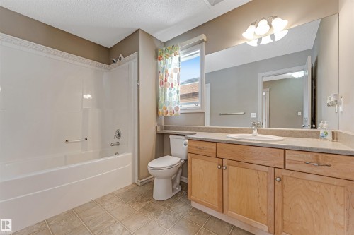 Bathroom featuring a full tub and shower combination with white surround, a light wood-finish vanity with an integrated sink and light-toned countertop, a large mirror, and tiled flooring - 1431 Hodgson Way, Edmonton, AB - Indoor Photo Showing Bathroom