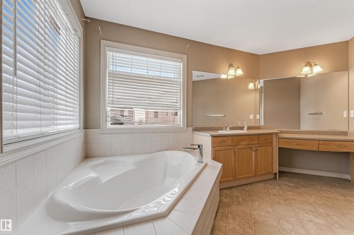Corner soaking tub with white tile surround, adjacent to dual windows - 1431 Hodgson Way, Edmonton, AB - Indoor Photo Showing Bathroom