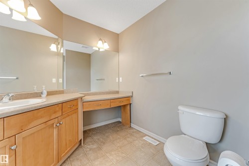 Bathroom featuring a single basin vanity with wood cabinetry, a built-in makeup vanity, large wall-mounted mirrors, and tiled flooring - 1431 Hodgson Way, Edmonton, AB - Indoor Photo Showing Bathroom
