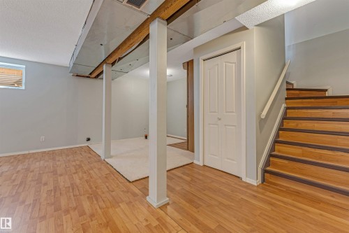 Open basement area featuring wood-finish flooring, light grey walls, white bi-fold closet doors, and wood stairs with a white handrail - 1431 Hodgson Way, Edmonton, AB - Indoor Photo Showing Other Room