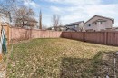 Expansive rear yard featuring a wooden privacy fence, established grass, and mature trees beyond the fence line - 1431 Hodgson Way, Edmonton, AB  - Outdoor 