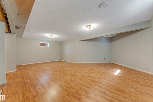 Spacious basement room featuring wood-finish flooring, light gray painted walls, and overhead flush mount lighting fixtures - 1431 Hodgson Way, Edmonton, AB - Indoor