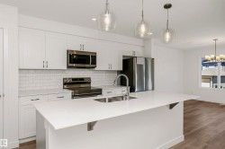 Modern kitchen featuring an oversized island with an undermount sink, white shaker cabinetry, stainless steel appliances, a subway tile backsplash, and overhead pendant lighting - 