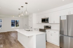 Contemporary kitchen featuring a center island with sink, white shaker cabinetry, white subway tile backsplash, stainless steel appliances, and wood-finish flooring - 