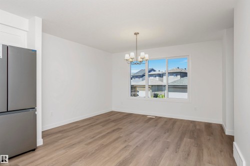 Spacious room featuring wood-finish flooring, a large window, and a contemporary chandelier - 9552 Carson Bend Bend, Edmonton, AB - Indoor Photo Showing Other Room