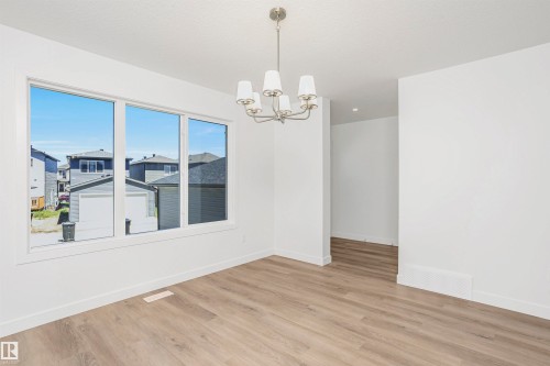 Spacious room featuring light wood-finish flooring, a contemporary chandelier, white walls, and a large triple window - 9552 Carson Bend Bend, Edmonton, AB - Indoor Photo Showing Other Room