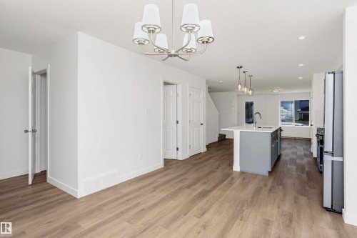 Open-concept living area featuring wood-finish flooring, a modern chandelier, and a kitchen island with pendant lighting - 9552 Carson Bend Bend, Edmonton, AB - Indoor Photo Showing Kitchen