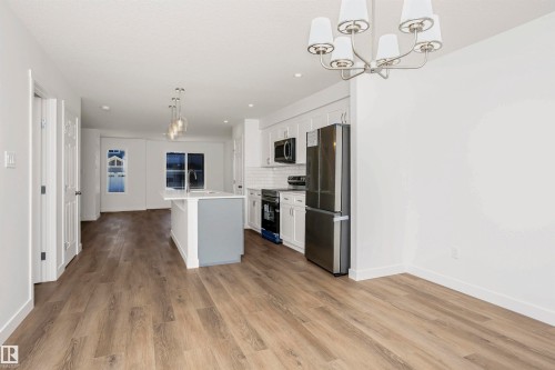 Open-concept main living area with wood-finish flooring, a contemporary kitchen island with a quartz countertop, white shaker cabinetry, stainless steel appliances, and a modern chandelier - 9552 Carson Bend Bend, Edmonton, AB - Indoor Photo Showing Kitchen