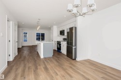 Open-concept main living area with wood-finish flooring, a contemporary kitchen island with a quartz countertop, white shaker cabinetry, stainless steel appliances, and a modern chandelier - 