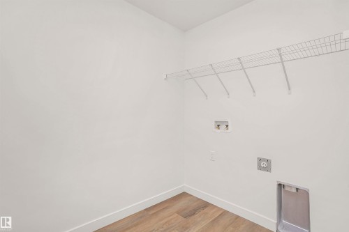 Dedicated laundry space featuring wood-finish flooring, white walls, and a built-in wire shelf - 9552 Carson Bend Bend, Edmonton, AB - Indoor With Storage